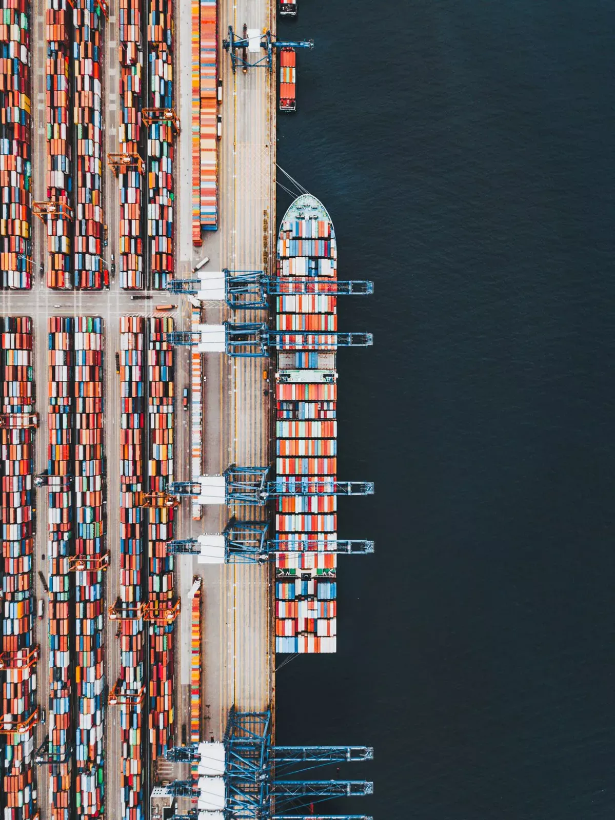 Vista aérea de un buque portacontenedores atracado junto a grúas pórtico en una terminal portuaria